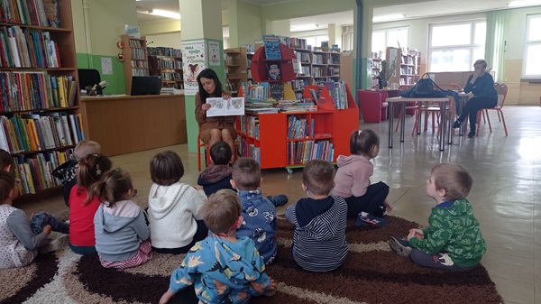 dzieci siedząc na dywanie słuchają czytanej przez bibliotekarkę książki